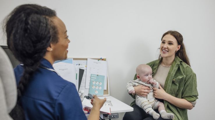 Medical assistant talking with a young mother holding a baby